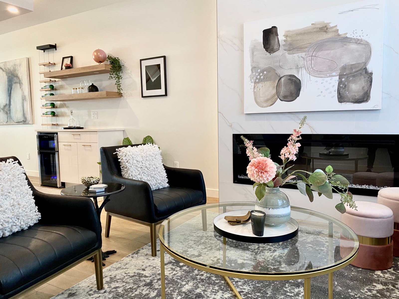 Living room styled by Aimee Lauren Interiors with black leather chairs, a glass coffee table, and abstract artwork over the fireplace